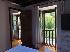 Une chambre avec un lit, une porte en bois et un balcon donnant sur un paysage verdoyant.