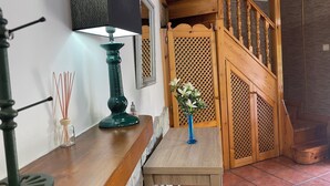 A wooden staircase with a wooden railing, a table with a vase of flowers, and a lamp on a wall. - La Casina del Arroyo, rural cottage for 2-4 people in Poo de Cabrales (Póo de Cabrales)