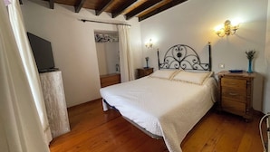 A bedroom with a wooden ceiling, a bed with a white bedspread, a nightstand with a lamp, and a dresser. - La Casina del Arroyo, rural cottage for 2-4 people in Poo de Cabrales (Póo de Cabrales)