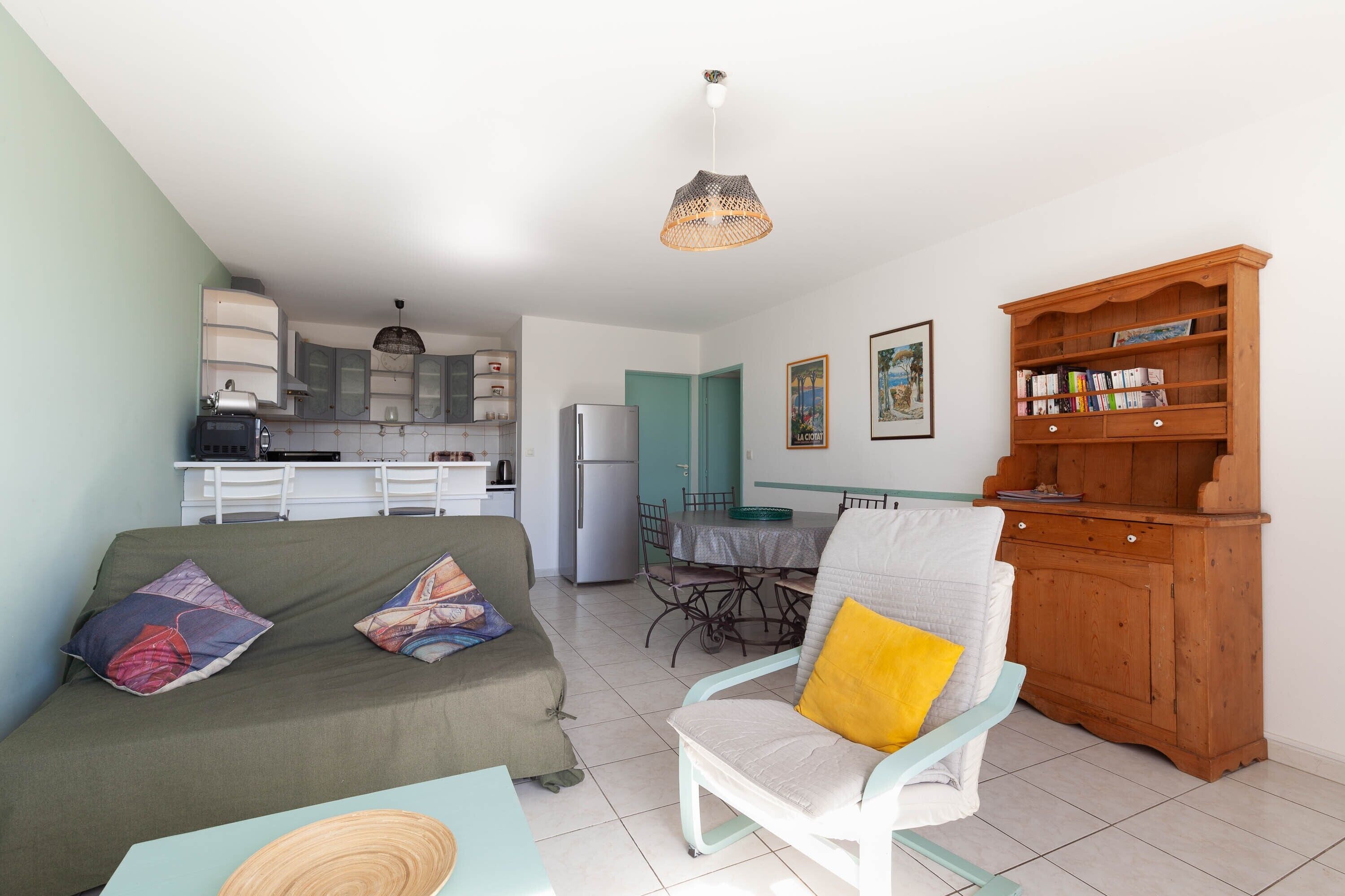 Un salon avec un canapé, un fauteuil, un meuble en bois, une table à manger et, au fond, une cuisine.