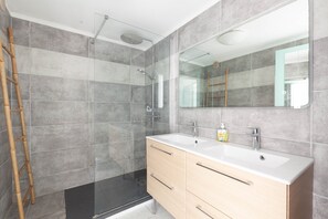 Une salle de bain moderne dotée d’une douche à parois de verre, d’un grand miroir et d’un meuble-lavabo à deux vasques.