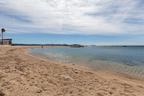 Une plage à l’eau claire, un poste de surveillance des sauveteurs et des montagnes qui se dessinent à l’horizon.