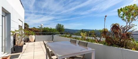 Una terraza en la azotea con una mesa y sillas, plantas en macetas y vistas de la ciudad.