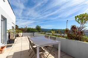 Une terrasse sur le toit, avec une table et des chaises, des plantes en pot et une vue sur la ville.