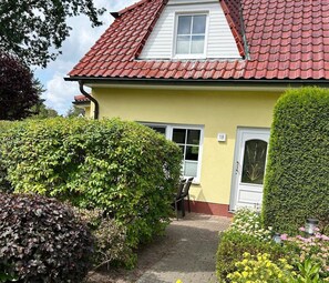 Une maison jaune avec un toit recouvert de tuiles rouges, une porte blanche et le numéro « 18 » peint sur le mur.