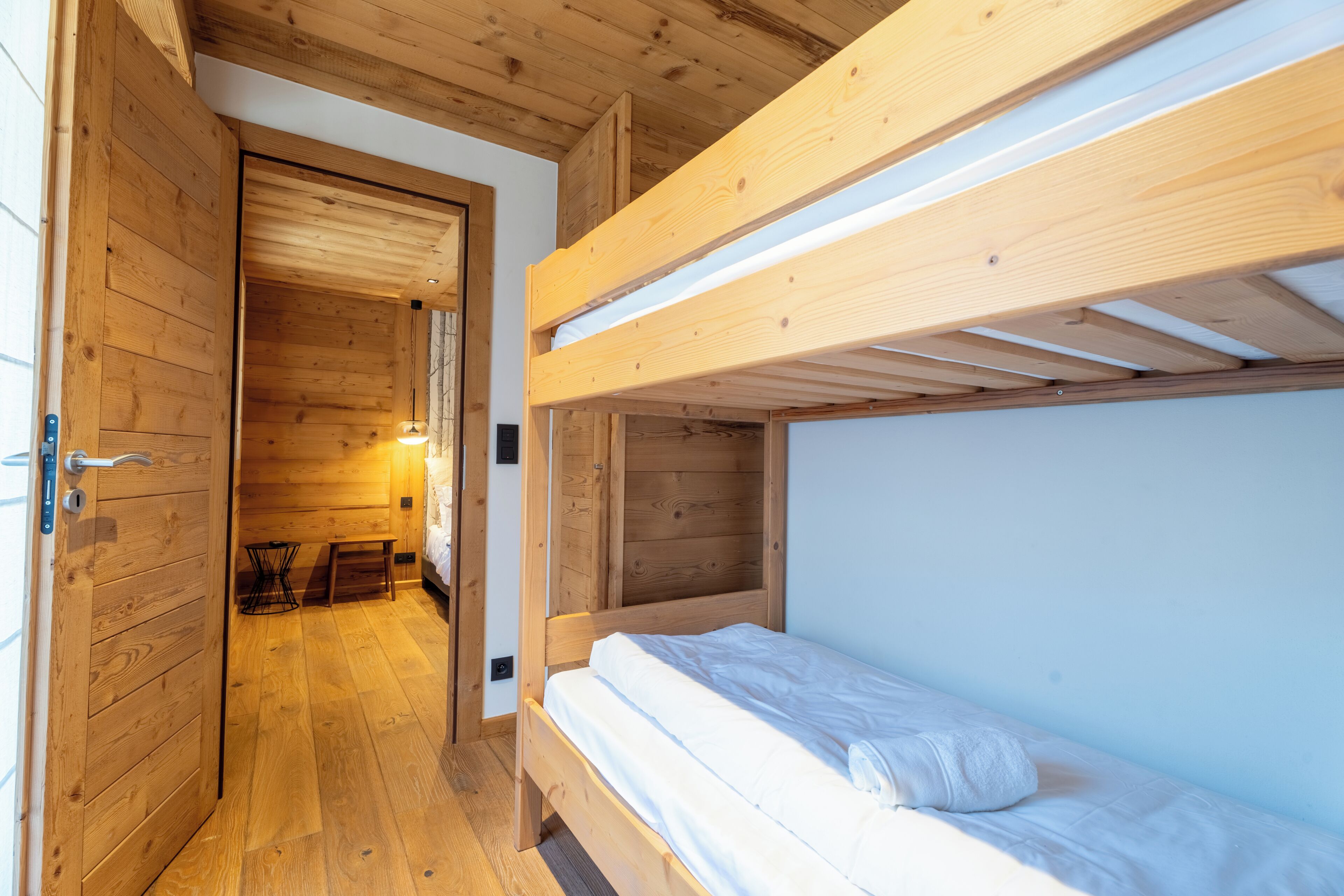 A bunk bed room with wooden walls and floors, a door, and a small table.
