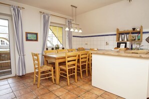 A kitchen with a wooden dining table, chairs, a tiled backsplash, and a wooden shelf with kitchen items. - Spacious vacation apartment with terrace and garden in the quiet Landhaus Wildrose - (Zirkow)