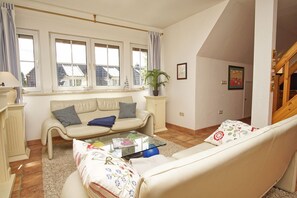 A living room with a sofa, a coffee table, and a window with curtains. - Spacious vacation apartment with terrace and garden in the quiet Landhaus Wildrose - (Zirkow)