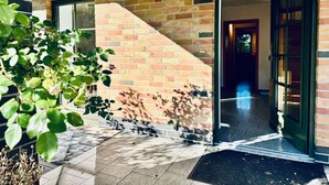 A building entrance with a brick facade, a glass door, and a tiled pathway leading to the door.