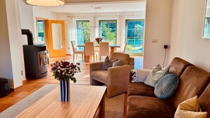 A cozy living room with a sofa, a wooden coffee table, and a vase of flowers. There is a fireplace and a dining area with chairs and a table.
