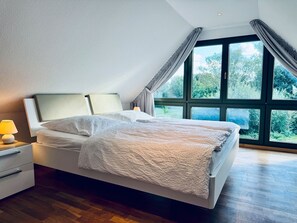 A modern bedroom with a large bed, a nightstand, and a window with curtains. - Ferienhaus Boddenblick - Charming semi-detached house in Trips on Rügen - (Bergen auf Rügen)