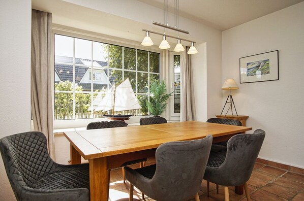 A dining area with a wooden table, four grey upholstered chairs, a sailboat model, and a lamp on a tripod.