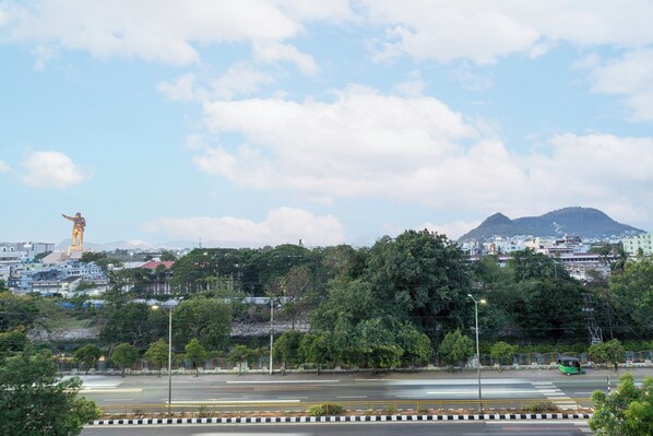 A cityscape with a prominent statue, a mountain, and a green bus on the road. - Itsy Hotels M (Vijayawada)
