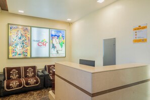 A hotel reception area with a reception desk, two sofas, and framed artwork on the walls. - Itsy Hotels M (Vijayawada)