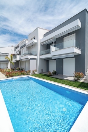 A modern residential building with a swimming pool, multiple balconies, and a well-maintained garden.