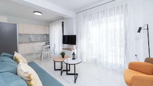 Un salon moderne avec un canapé, une petite table et un fauteuil. On y trouve également un coin cuisine avec des placards et un téléviseur.