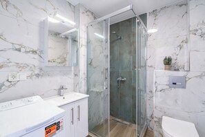 Ein Badezimmer mit einer gläsernen Duschkabine, einem weißen Waschbecken und einer Wand mit Marmorfliesen.