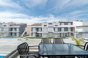 Un bâtiment moderne doté de nombreux balcons, d’une piscine et d’un espace extérieur aménagé pour s’asseoir.