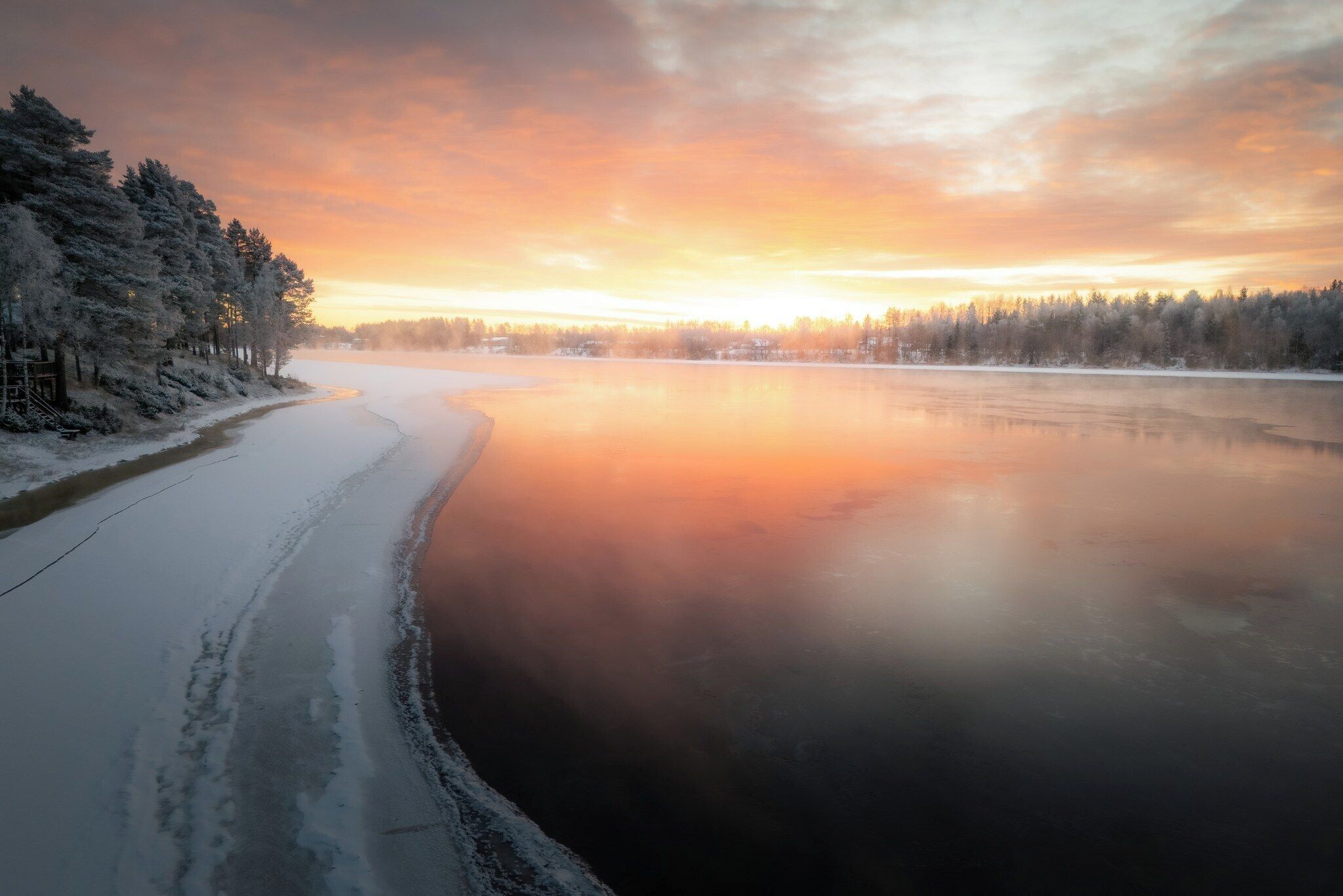 A frozen river with snow-covered trees and a clear sky.