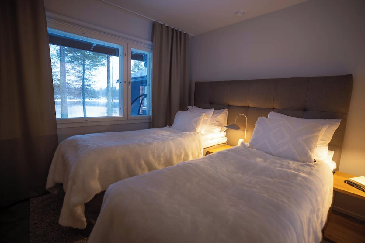 Une chambre d’hôtel avec deux lits, une grande fenêtre et une vue sur les arbres.