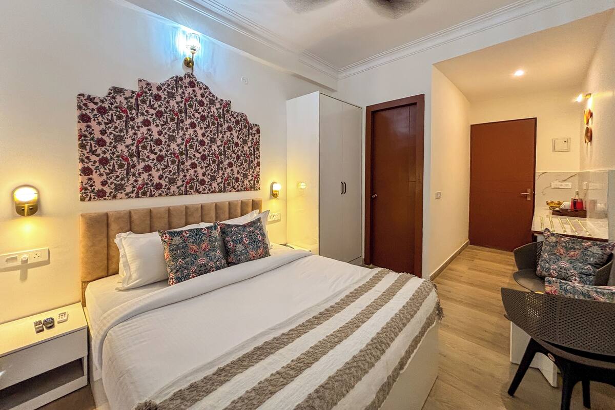 A hotel room with a bed, a headboard with floral wallpaper, a ceiling fan, and a desk with a chair.