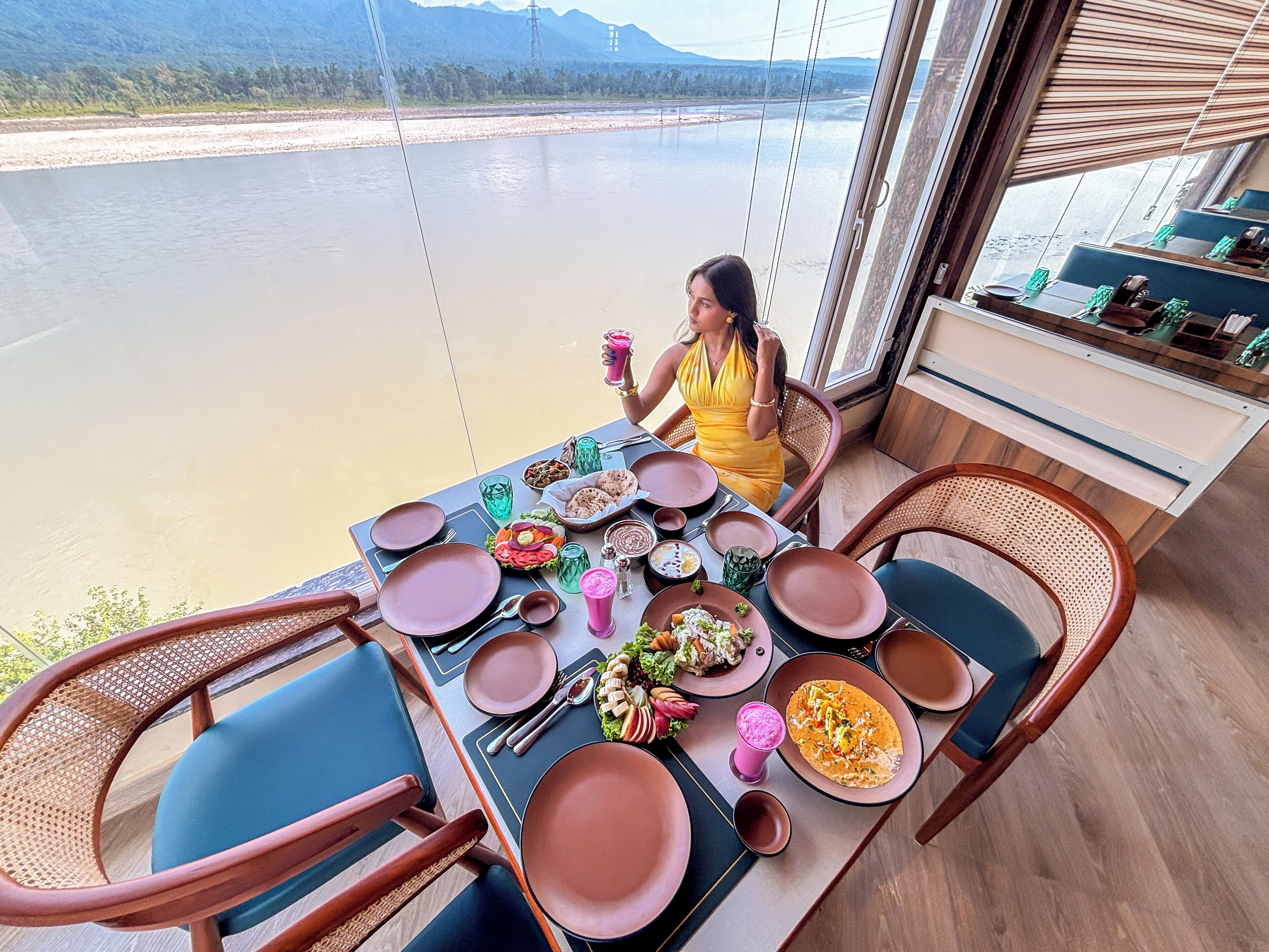 Une table à manger dressée avec des assiettes, des bols et des verres, donnant sur une rivière.