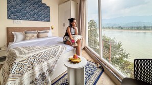 Hotelkamer met een groot bed, een klein tafeltje met fruit, uitzicht op een rivier en een behang met patroon.