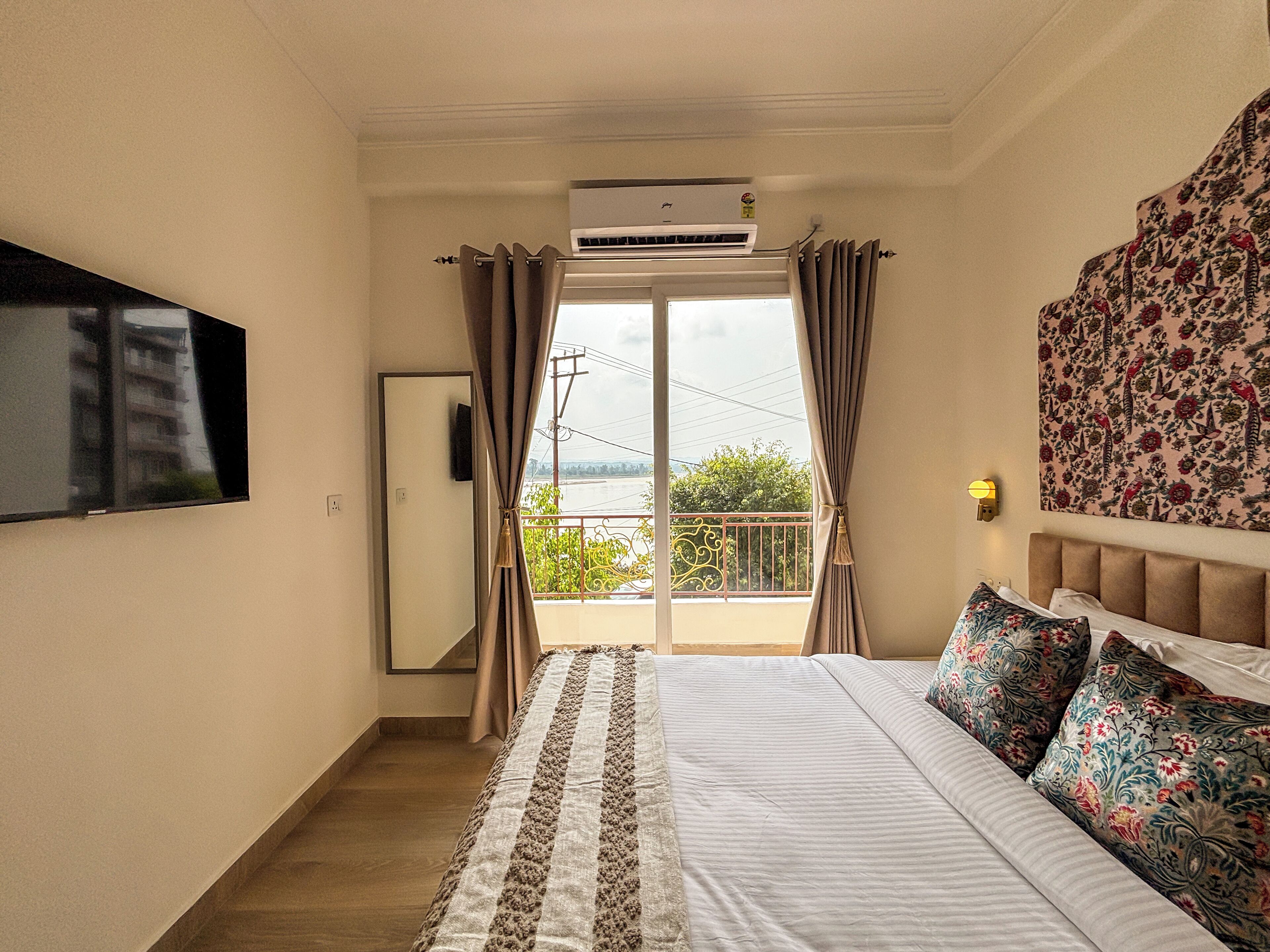 A bedroom with a bed, a TV mounted on the wall, and a balcony with curtains.