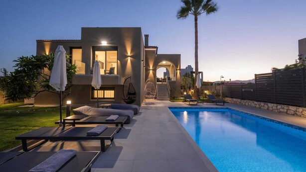 Un espace moderne aménagé au bord de la piscine, avec des chaises longues, une piscine et un bâtiment bien éclairé doté d’un balcon.