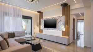 Un salon moderne avec un grand téléviseur à écran plat fixé sur un meuble blanc, un canapé beige et une table basse en verre.