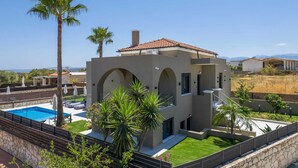 Une maison moderne à deux étages, dotée d’une piscine, de palmiers et offrant une vue sur les montagnes.