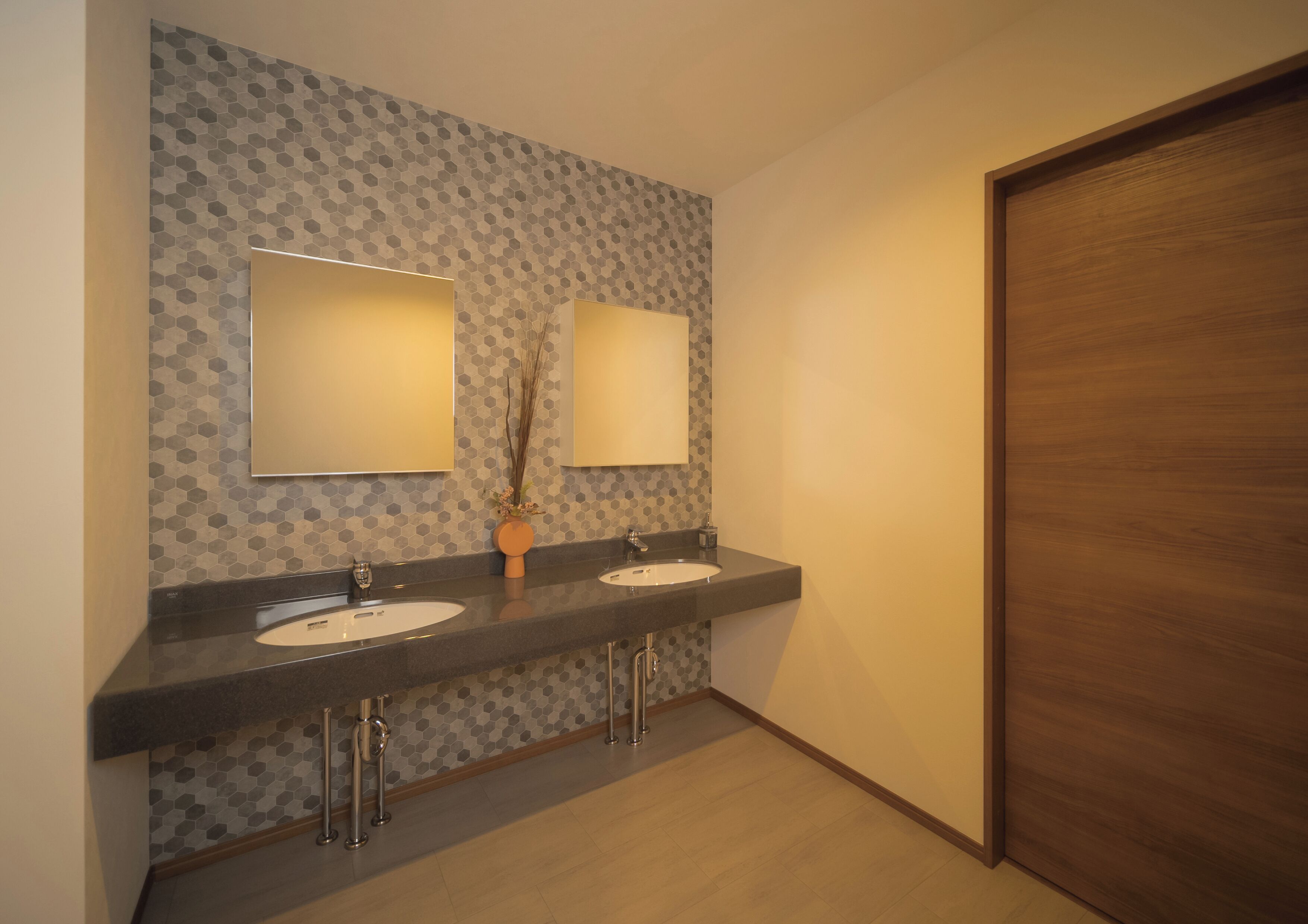 Een badkamer met twee wastafels, elk met een spiegel erboven, en een houten deur.