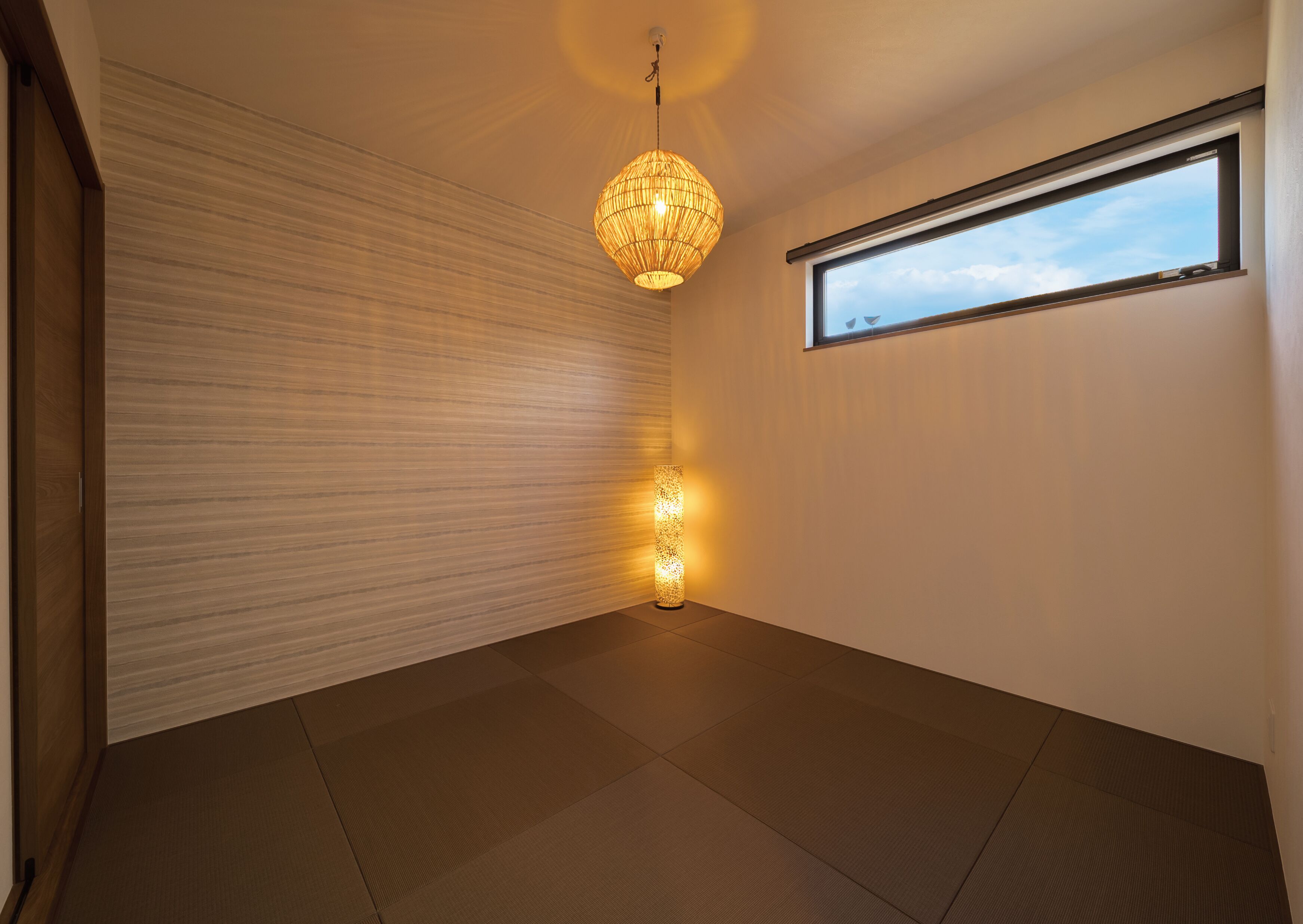 Une pièce au décor minimaliste, dotée d’une grande fenêtre, d’un luminaire suspendu et d’un mur à texture.