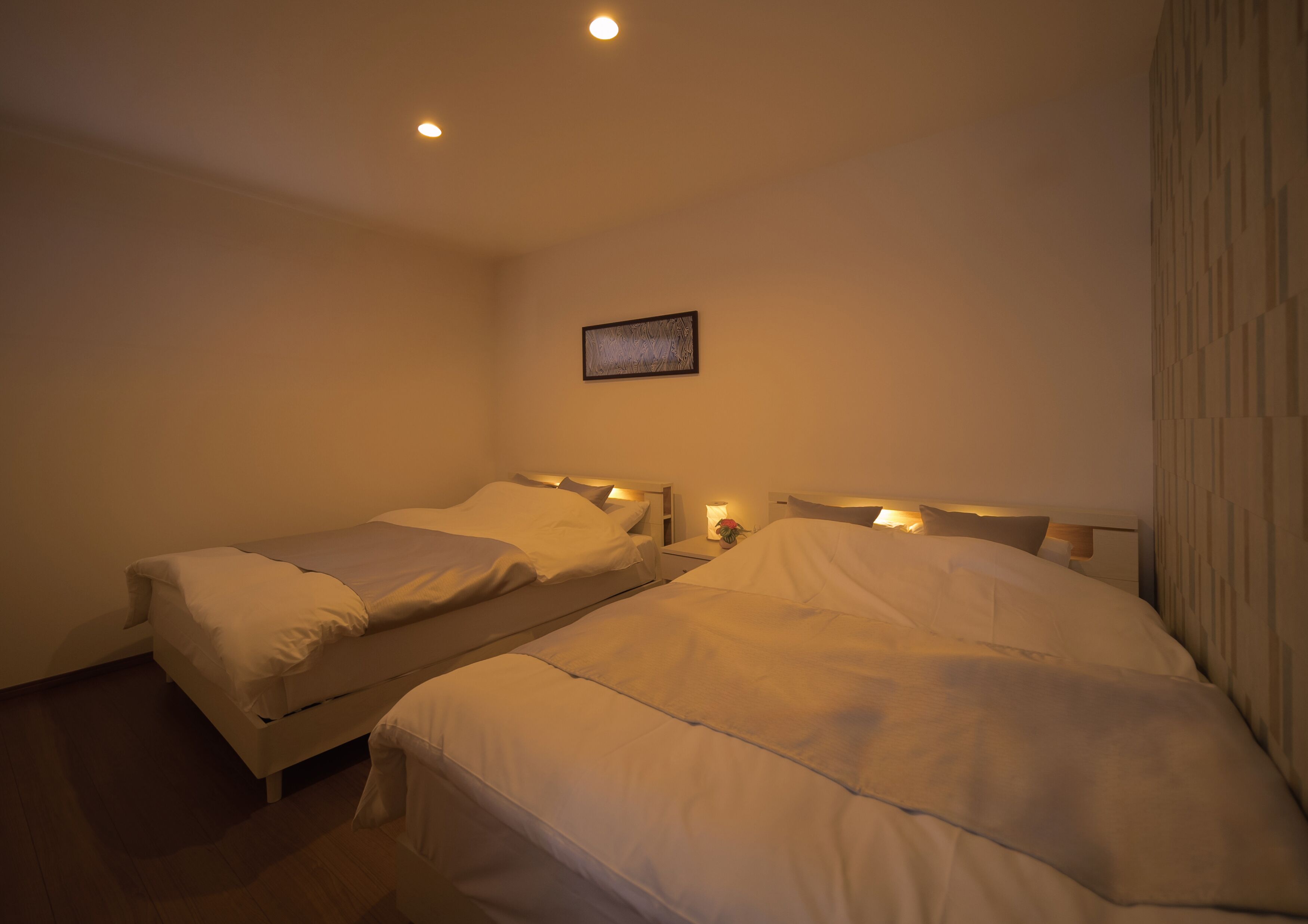 A hotel room with two single beds, a small bedside table with a lamp, and a framed picture on the wall.