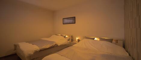 A hotel room with two single beds, a small bedside table with a lamp, and a framed picture on the wall.
