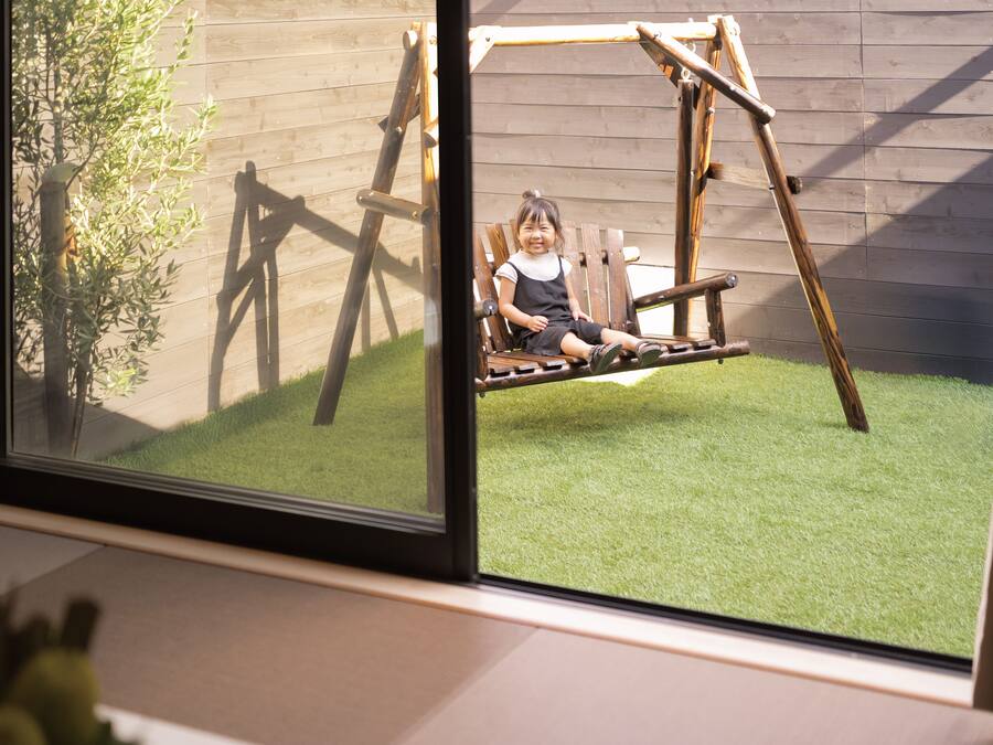 Niño en un columpio de madera en un patio trasero con césped artificial y valla de madera.