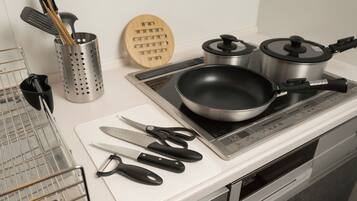 A kitchen with a stove, pots, a frying pan, a cutting board, and various utensils.