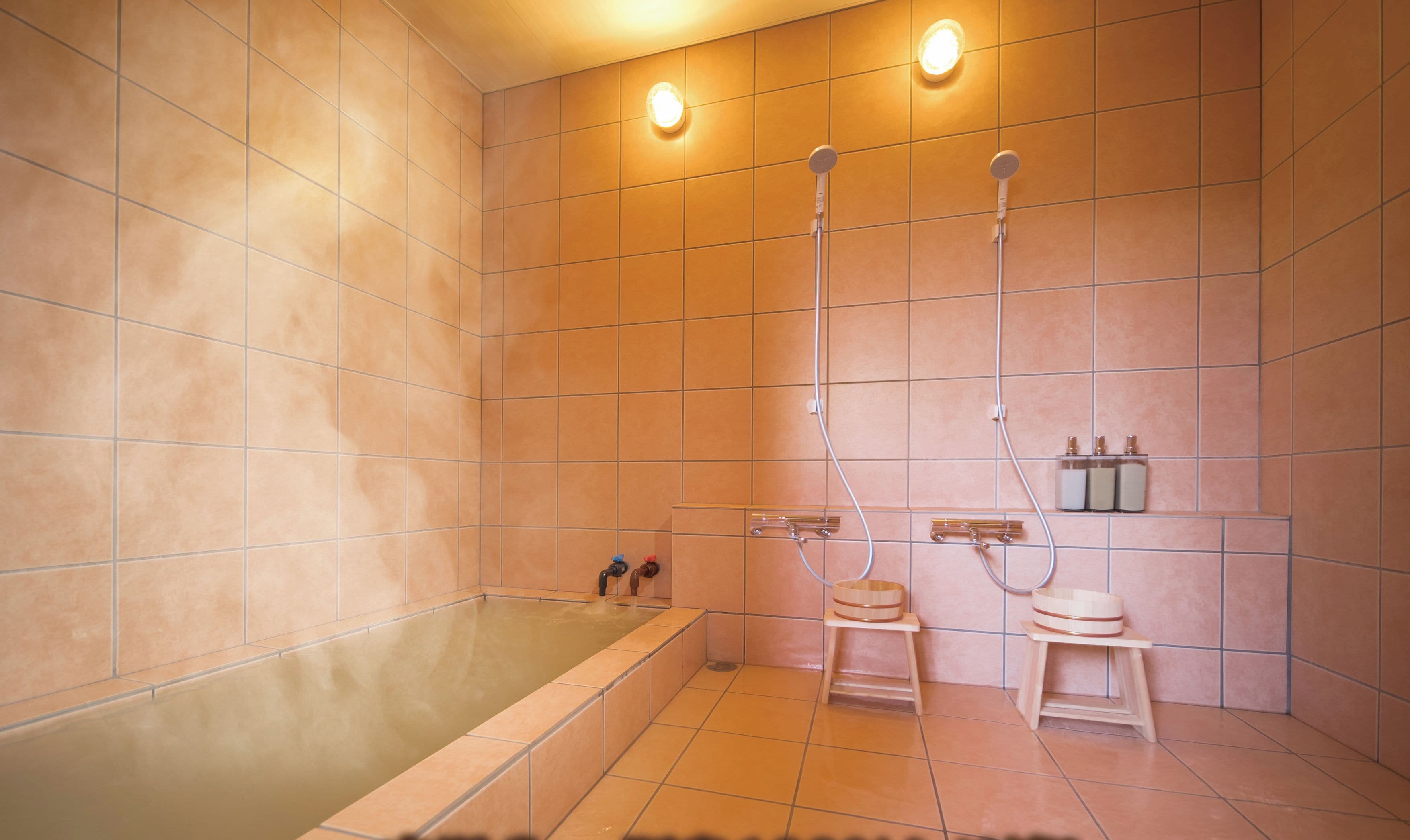 A modern bathroom with a large bathtub, two showerheads, and a wooden stool.