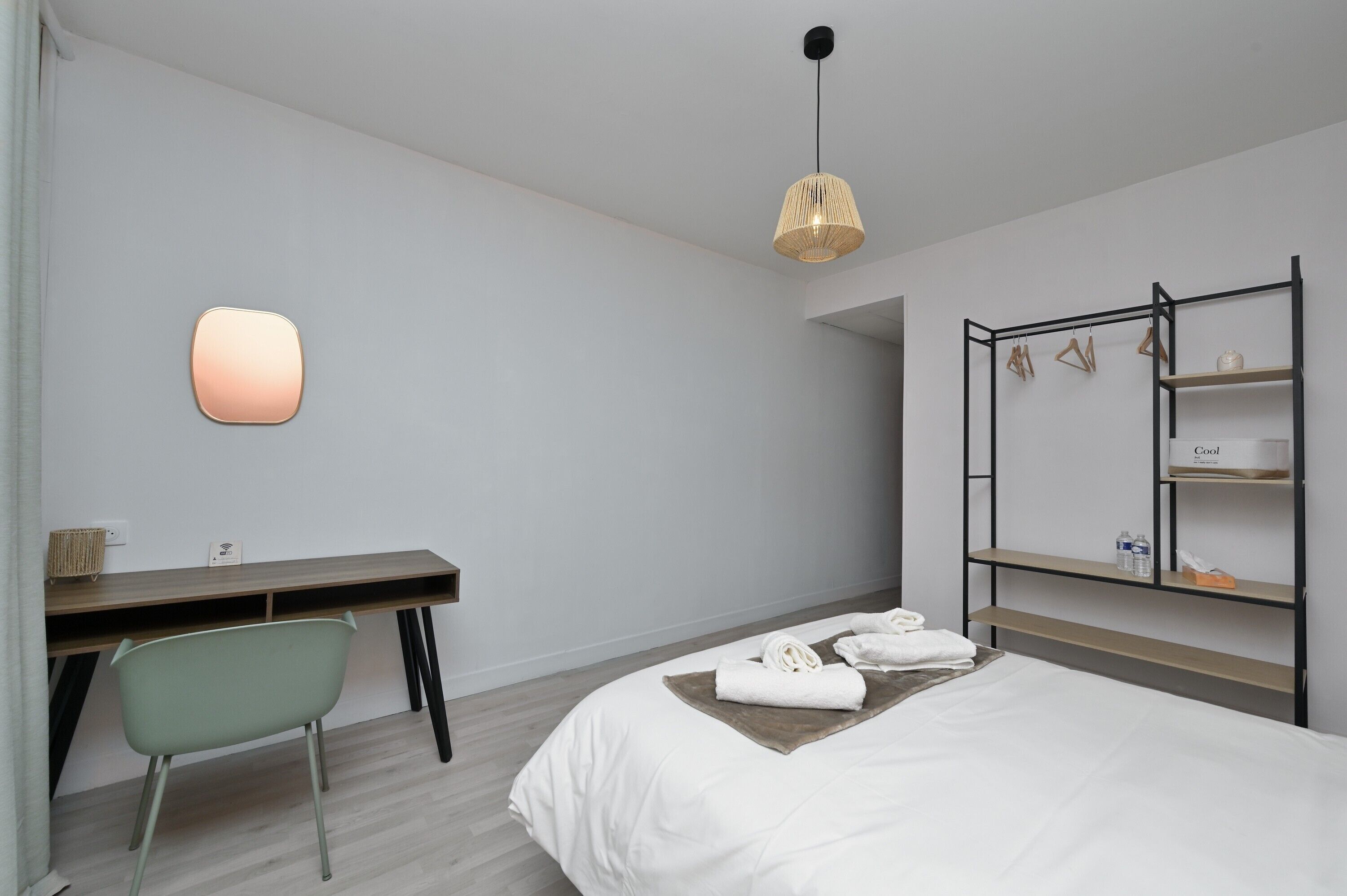 Quarto de hotel com cama, escrivaninha, cadeira, luminária pendente e armário embutido.