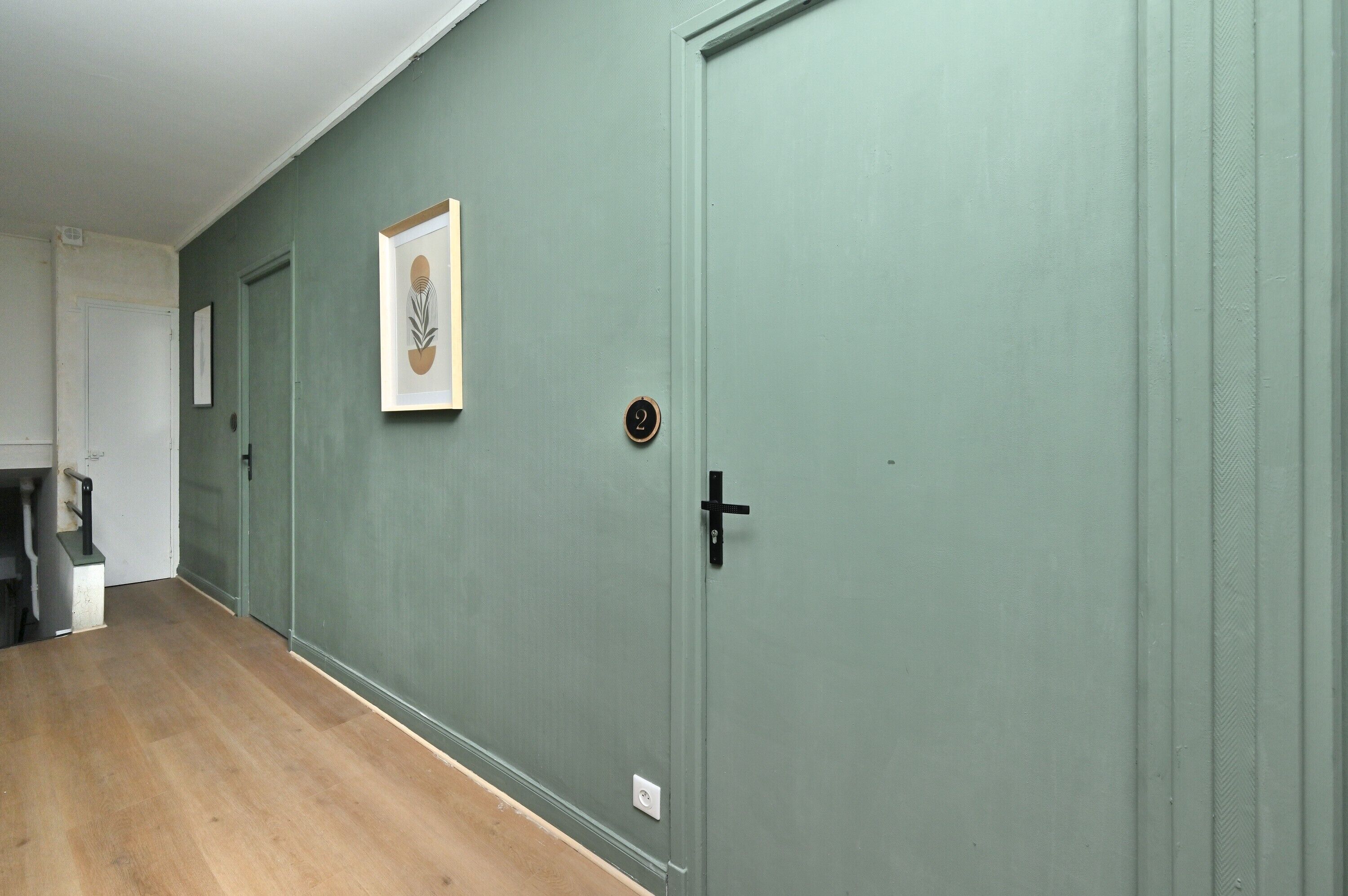 Un pasillo con una puerta verde, un cuadro en la pared y un cubo de basura.