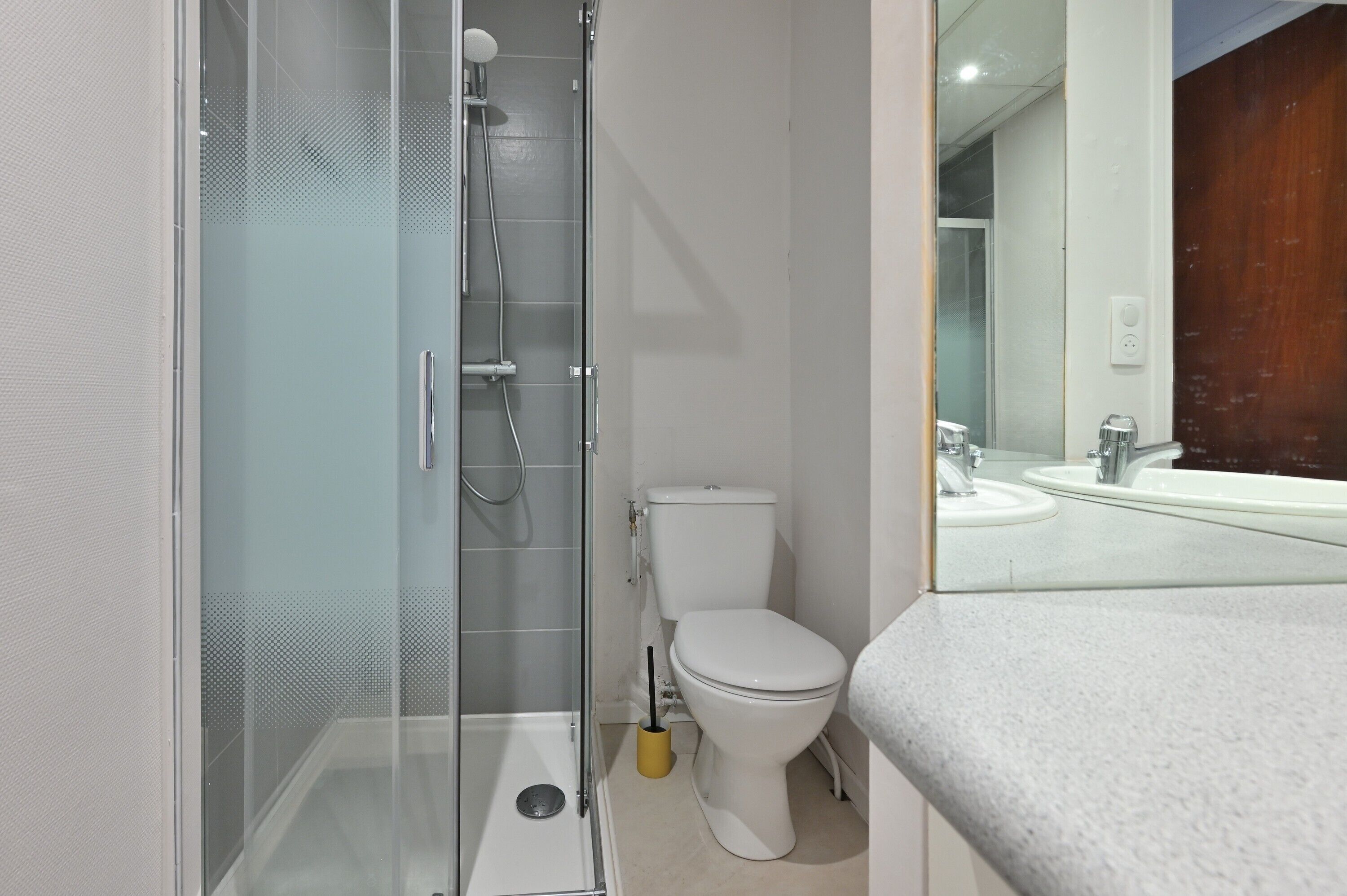 A bathroom with a glass shower enclosure, a toilet, and a sink with a mirror.