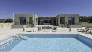 Un espace piscine extérieur moderne, doté d’un coin salon et offrant une vue dégagée sur la piscine.