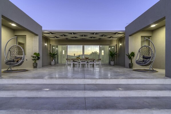 A modern outdoor patio with a dining area, two hanging chairs, and potted plants. - Villa Navelina, Villa (Chania)