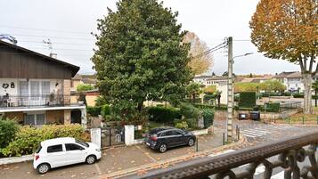 Rua residencial com carros estacionados, uma grande árvore e casas.