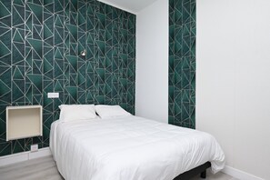 A bedroom with a geometric-patterned wall, a bed with white bedding, a bedside table, and a wall-mounted light. - Room 'Double Room' with Shared Terrace, Wi-Fi and Air Conditioning (Salies-du-Salat)