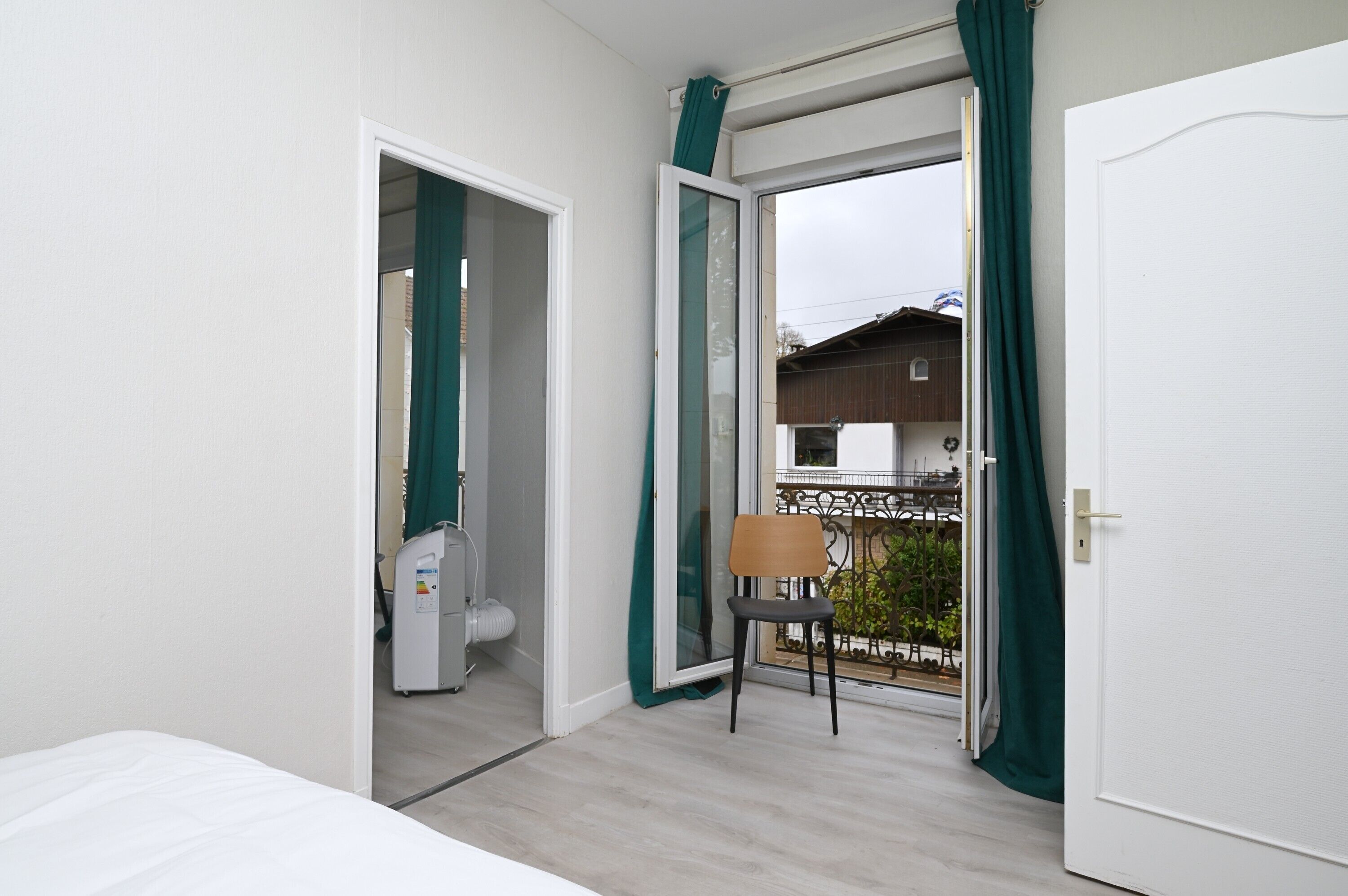 A room with a bed, a chair, a sliding glass door leading to a balcony, and a white door.