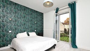 Une chambre avec un mur orné d’un motif géométrique, un lit, un radiateur et une porte-fenêtre coulissante donnant sur un balcon.