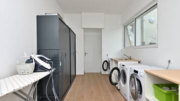 Une buanderie équipée d’un lave-linge, d’un sèche-linge, d’une planche à repasser et d’un étendoir.