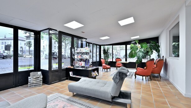 A modern interior with large windows, a sofa, red chairs, a small bookshelf, and a tiled floor. - Room 'Double Room' with Shared Terrace, Wi-Fi and Air Conditioning (Salies-du-Salat)