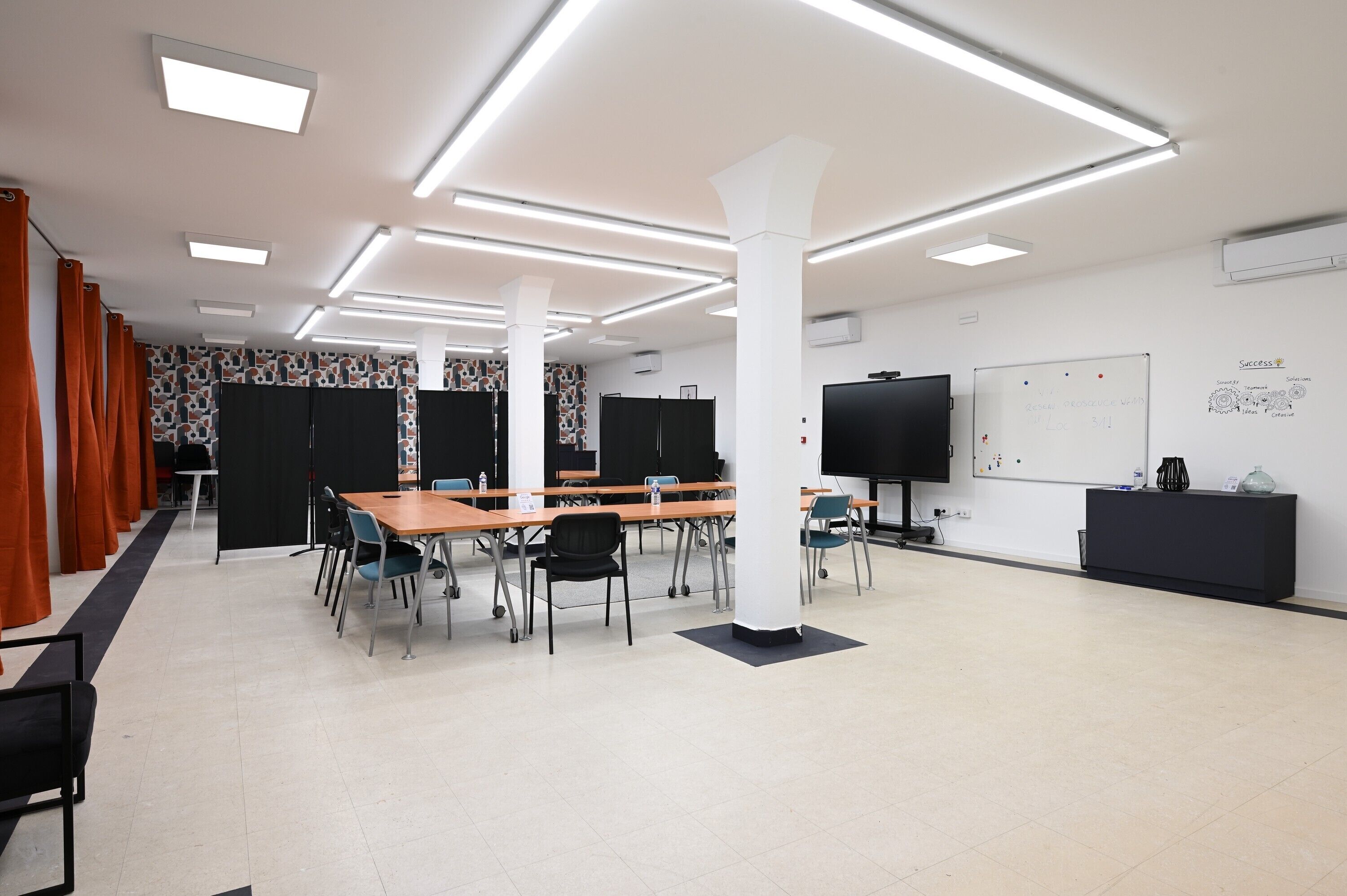 A conference room with tables, chairs, a whiteboard, and a TV screen.